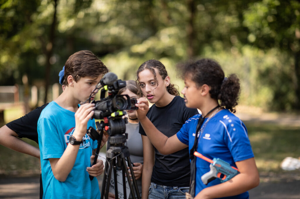 Jugendliche versammeln sich um eine Kamera auf einem Stativ beim Außendreh.