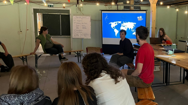 Dokumentarfilmworkshop; Cosima Lange vor Tafel mit Weltkarte, Schüler:innen im Vordergrund
