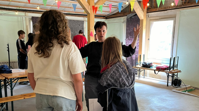 Dokumentarfilmworkshop; Cosima Lange hebt die Arme vor zwei Schüler:innen von hinten