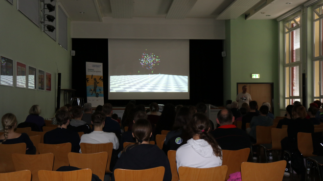 Vortrag Visuelle Effekte; Dozent mit Präsentation im Hintergrund über Köpfe