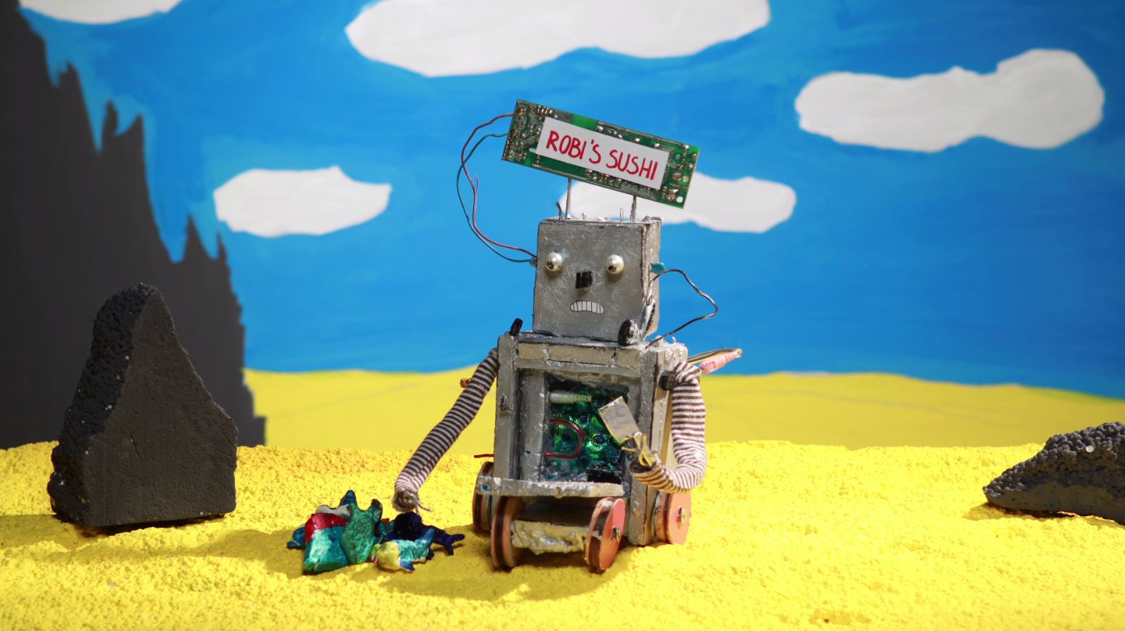 ein gebastelter Roboter auf gelben Untergrund vor einem blauen Himmel